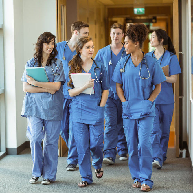 Group of healthcare professionals in blue scrubs walking down a hospital corridor.